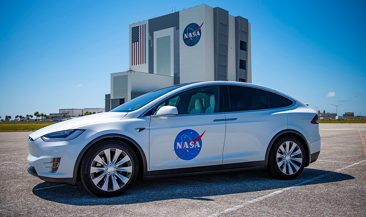 Tesla car with NASA logo signifying SpaceX ISS Mission Delays, parked in front of the Kennedy Space Center